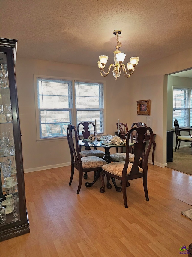 dining room with light wood-type flooring, an inviting chandelier, baseboards, and a textured ceiling