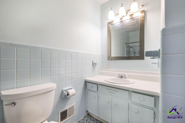 bathroom with visible vents, wainscoting, toilet, vanity, and tile walls