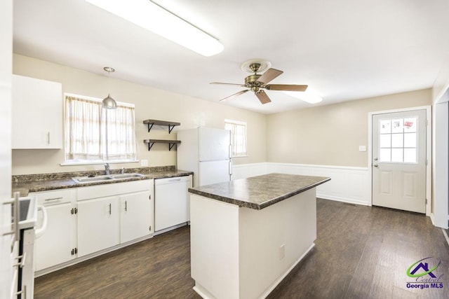 kitchen with dark countertops, white cabinets, a kitchen island, a sink, and white appliances