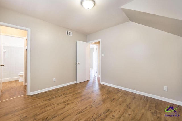 unfurnished bedroom with lofted ceiling, connected bathroom, wood finished floors, visible vents, and baseboards