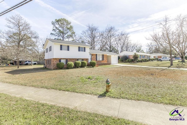 split level home featuring an attached garage, driveway, brick siding, and a front yard