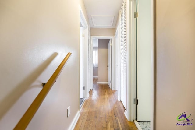 hall with attic access, light wood-type flooring, baseboards, and an upstairs landing