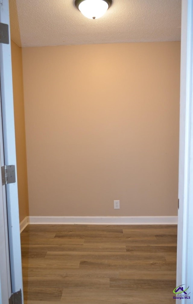 unfurnished room with a textured ceiling, baseboards, and wood finished floors