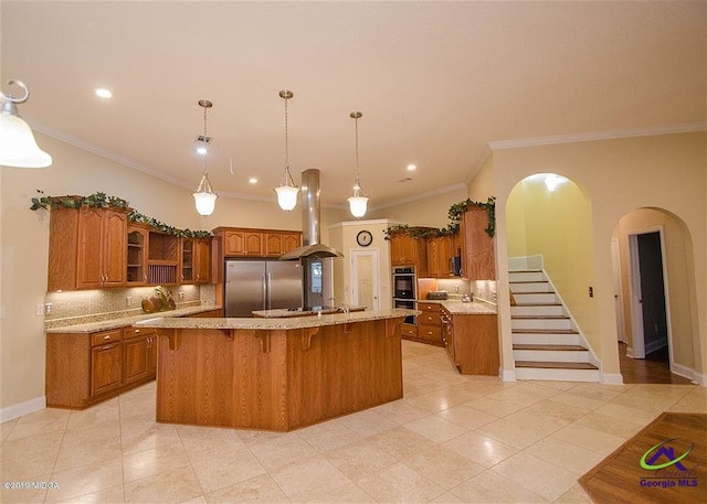 kitchen with stainless steel fridge, brown cabinetry, an island with sink, glass insert cabinets, and island exhaust hood