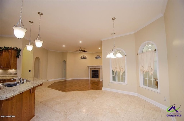 kitchen with arched walkways, brown cabinetry, open floor plan, light stone countertops, and a sink