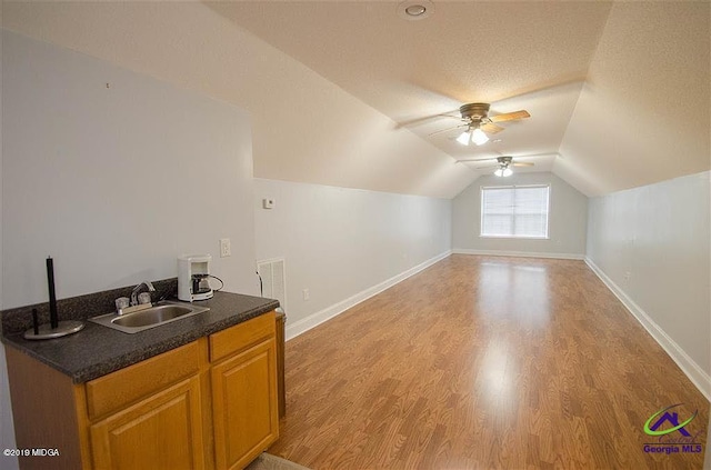 additional living space with light wood-type flooring, lofted ceiling, a sink, and baseboards