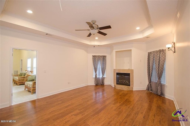 unfurnished living room featuring a tray ceiling, a fireplace, and wood finished floors