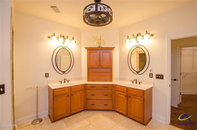 full bath with double vanity, visible vents, a walk in closet, and a sink