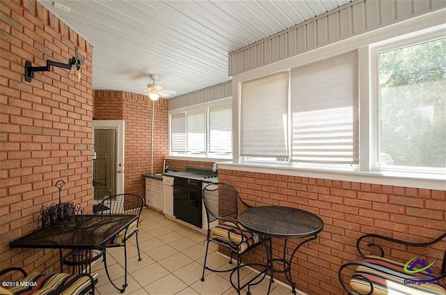 interior space with light tile patterned floors, brick wall, ceiling fan, and plenty of natural light