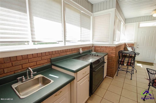 kitchen featuring light tile patterned flooring, black range with electric stovetop, a sink, white cabinets, and dark countertops