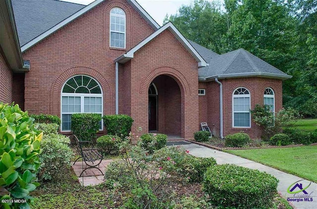 traditional-style house featuring brick siding, roof with shingles, and a front yard