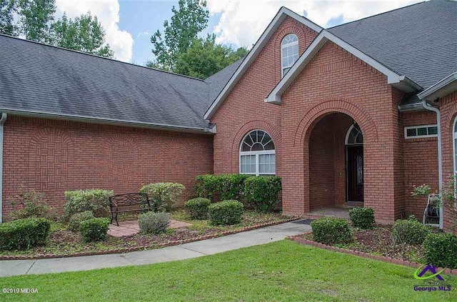 traditional-style house featuring brick siding, roof with shingles, and a front lawn