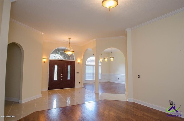 entryway with arched walkways, crown molding, light wood-style flooring, and baseboards