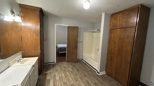 full bath with baseboards, ensuite bath, wood finished floors, a textured ceiling, and vanity