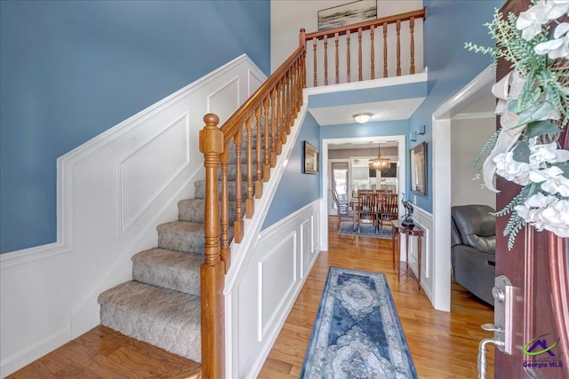 foyer entrance featuring a decorative wall, a wainscoted wall, a high ceiling, stairway, and light wood finished floors