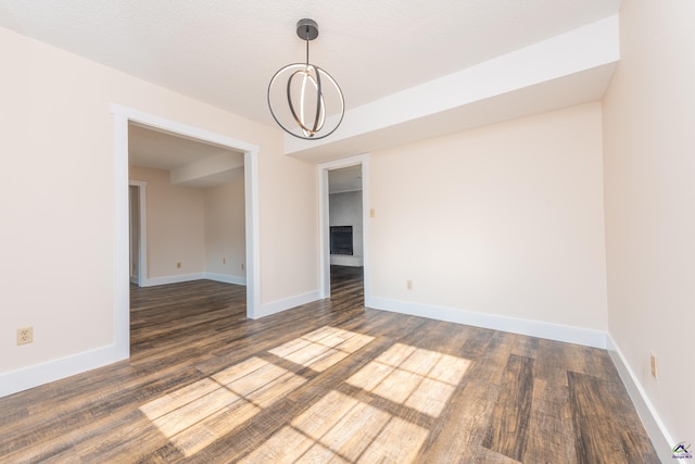 empty room featuring dark wood-style floors, a textured ceiling, a chandelier, and baseboards