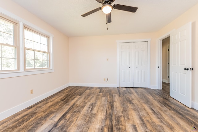 unfurnished bedroom featuring dark wood-style floors, a closet, baseboards, and a ceiling fan