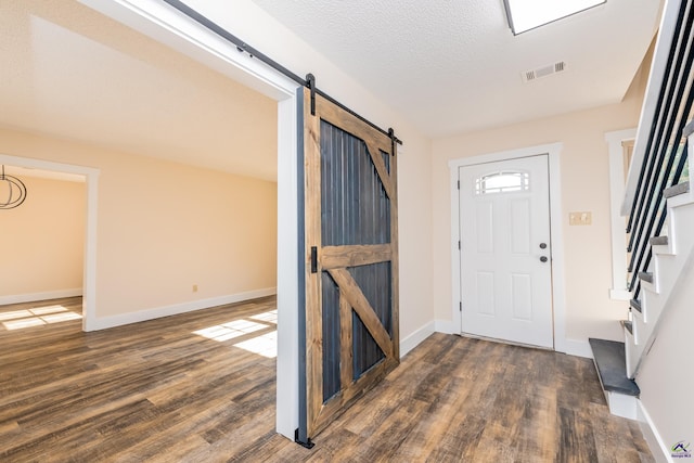 entrance foyer with dark wood-type flooring, a barn door, stairway, and visible vents