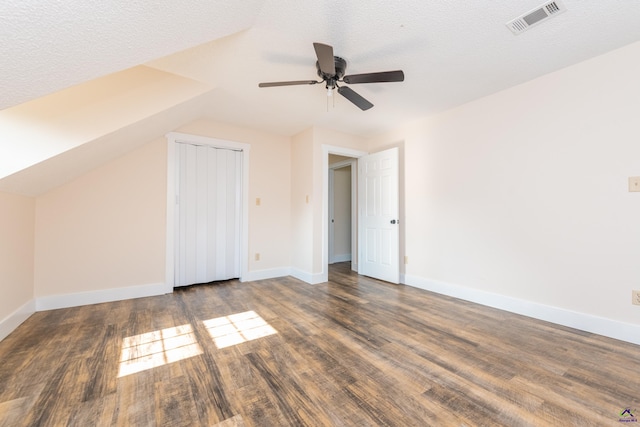 additional living space featuring baseboards, visible vents, dark wood finished floors, vaulted ceiling, and a textured ceiling