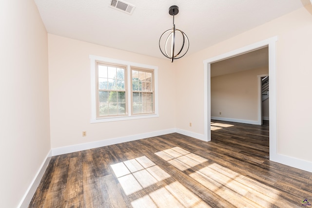 empty room with baseboards, visible vents, dark wood finished floors, and a notable chandelier