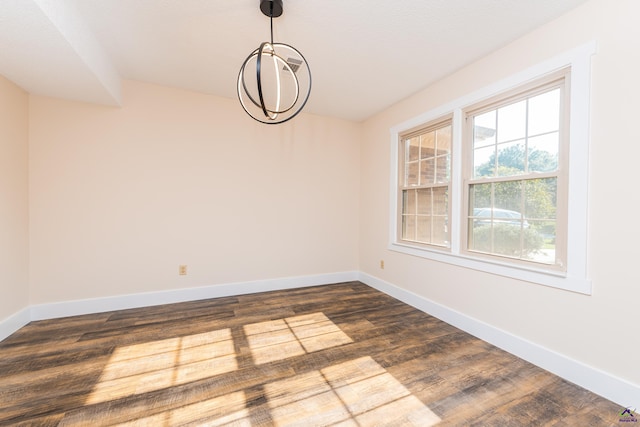 empty room with dark wood-style floors, a chandelier, and baseboards