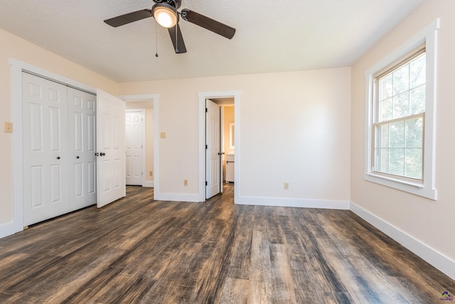 unfurnished bedroom with a textured ceiling, dark wood-style flooring, a closet, and baseboards