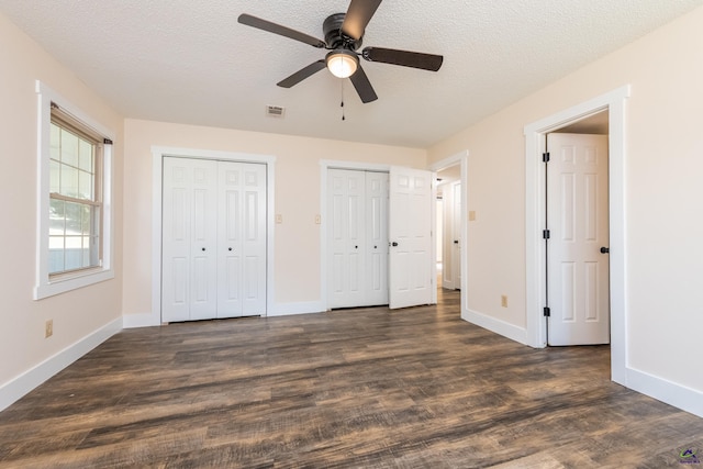 unfurnished bedroom featuring multiple closets, dark wood finished floors, a textured ceiling, and baseboards