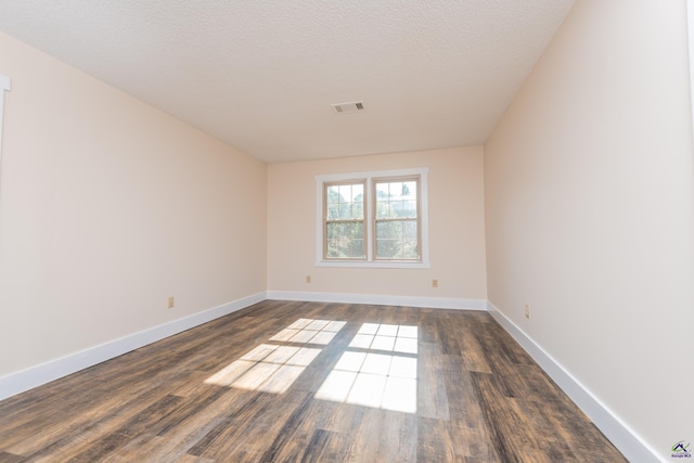 unfurnished room with dark wood-style floors, a textured ceiling, visible vents, and baseboards