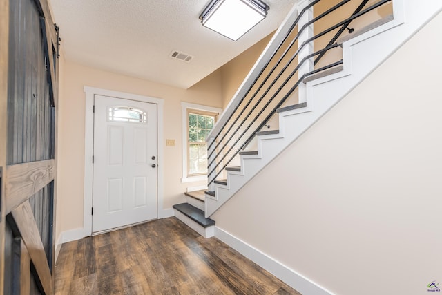 foyer featuring dark wood-style flooring, visible vents, a textured ceiling, baseboards, and stairs