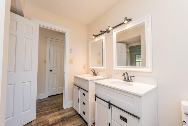 bathroom featuring wood finished floors, two vanities, a sink, and baseboards