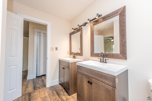 full bath with two vanities, a sink, baseboards, and wood finished floors