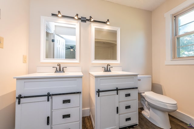 bathroom with two vanities, a sink, toilet, and wood finished floors