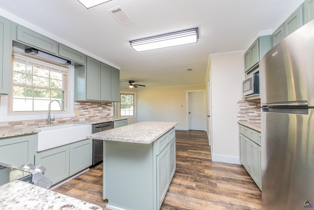 kitchen with visible vents, appliances with stainless steel finishes, a sink, a kitchen island, and light stone countertops