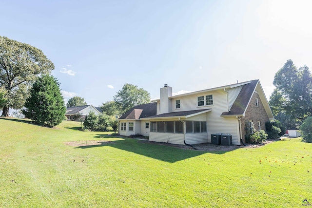 back of property with central AC unit, a lawn, a chimney, and a sunroom