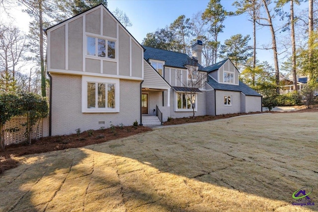 english style home with crawl space, brick siding, a chimney, and a front lawn