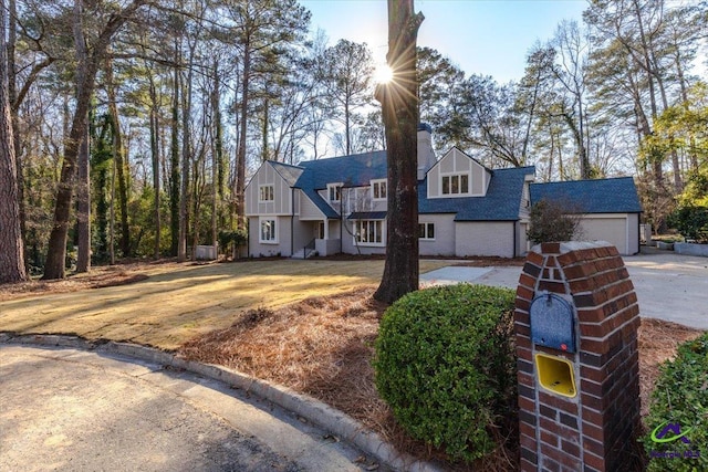 view of front of home with a garage, concrete driveway, a chimney, and roof with shingles