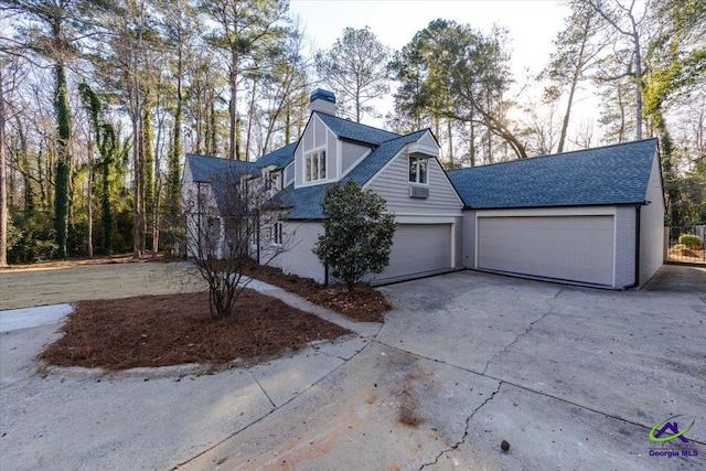 view of front of property featuring brick siding, a chimney, a shingled roof, an attached garage, and driveway