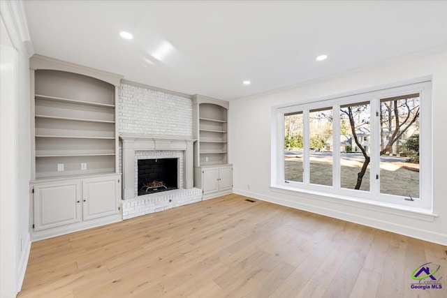 unfurnished living room with light wood finished floors, baseboards, crown molding, a fireplace, and recessed lighting