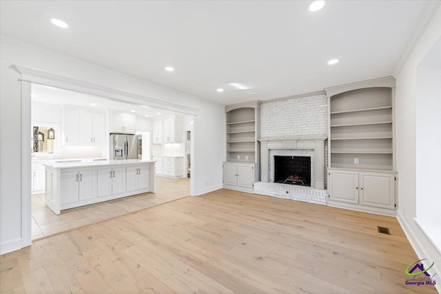 unfurnished living room featuring light wood-style floors, recessed lighting, a brick fireplace, and visible vents