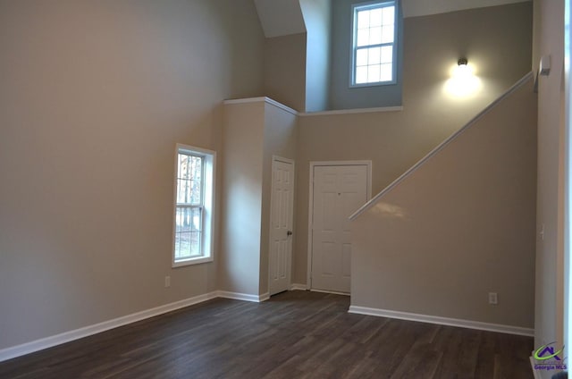 unfurnished living room with a high ceiling, dark wood-style floors, stairway, and baseboards