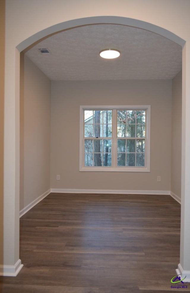 empty room with a wealth of natural light, visible vents, dark wood finished floors, and baseboards