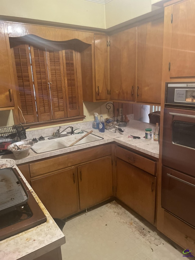 kitchen featuring a sink, light countertops, light floors, brown cabinetry, and cooktop