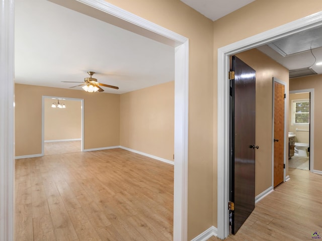 corridor with light wood-style flooring, attic access, and baseboards