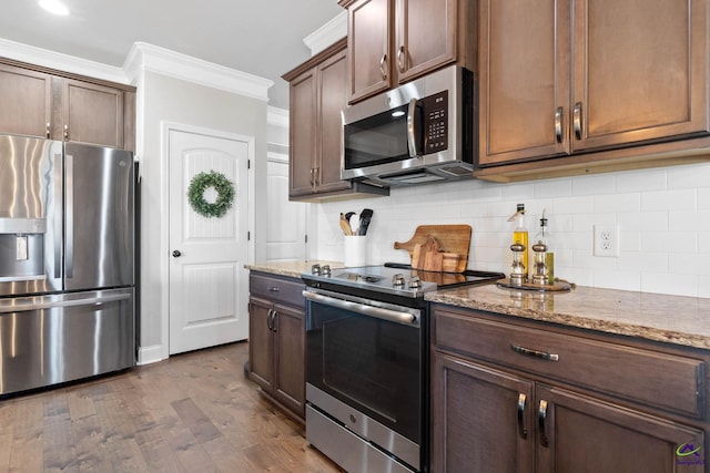 kitchen with appliances with stainless steel finishes, decorative backsplash, light stone counters, and ornamental molding