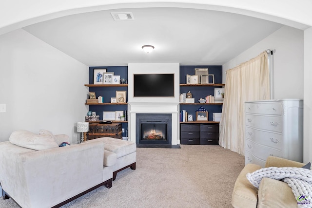 carpeted living room with a fireplace with flush hearth, visible vents, and arched walkways