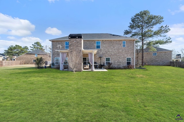 back of house featuring a patio, brick siding, a lawn, and fence