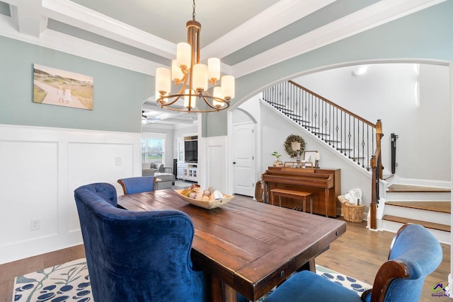 dining room featuring arched walkways, a notable chandelier, wainscoting, wood finished floors, and stairs