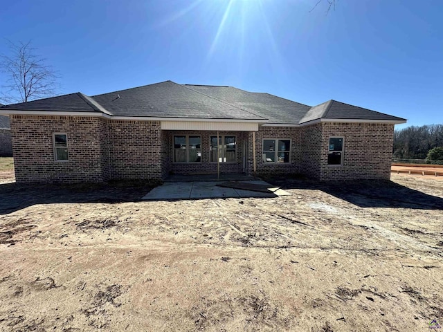 rear view of property with a shingled roof, brick siding, and a patio