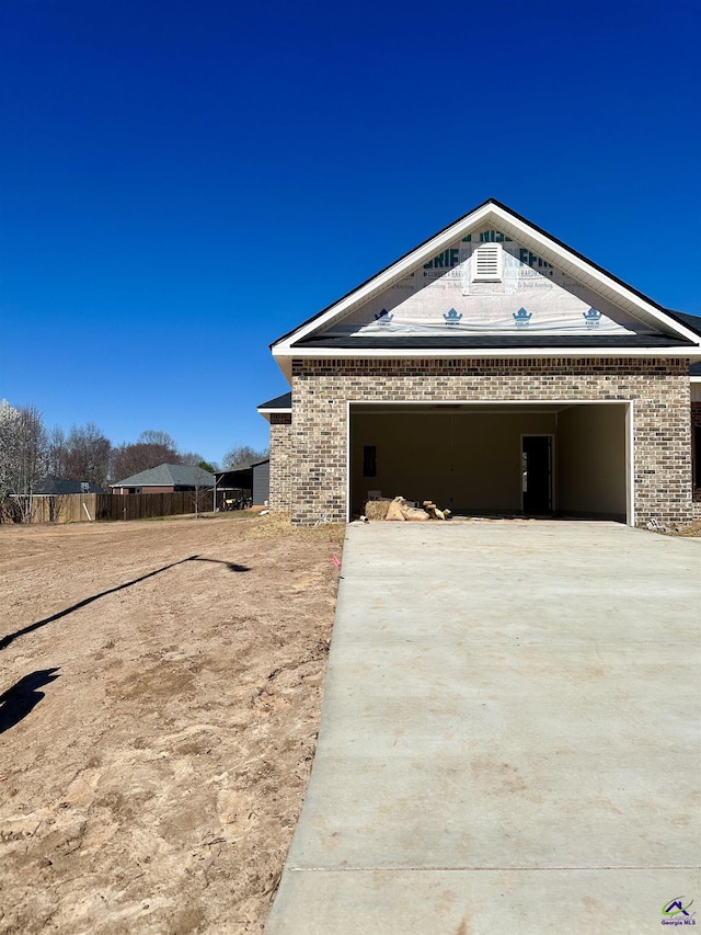 view of side of property featuring a garage, concrete driveway, brick siding, and fence