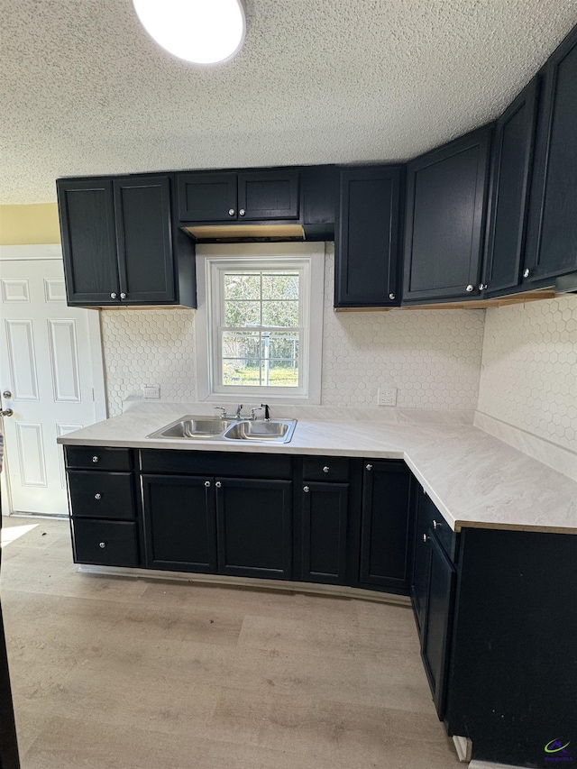 kitchen with light wood finished floors, decorative backsplash, light countertops, a textured ceiling, and a sink